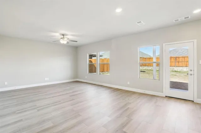 an empty room with wooden floor chandelier fan and windows