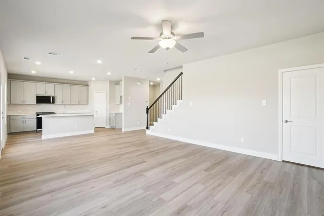 a view of an empty room with wooden floor and a ceiling fan