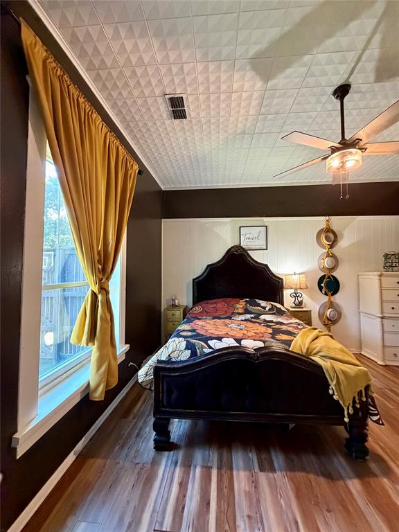 301 Forrest Avenue Cleburne, TX 76033 - Photo 11 of 14 Bedroom featuring wood-finish flooring, a textured ceiling with a central fan light fixture, and white beadboard wainscoting
