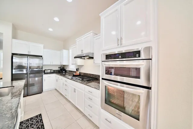 a kitchen with stainless steel appliances granite countertop a sink a stove and white cabinets with wooden floor