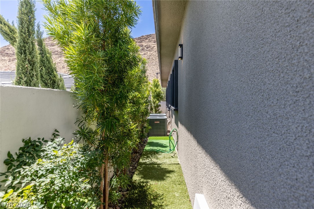 10118 Copper Edge Road Las Vegas, NV 89148 - Photo 43 of 48 A well-maintained side yard with lush greenery alongside a textured exterior wall, offering a serene outdoor passage.