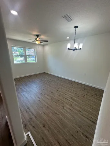 an empty room with wooden floor chandelier fan and windows