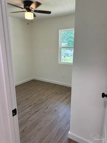 an empty room with wooden floor fan and windows