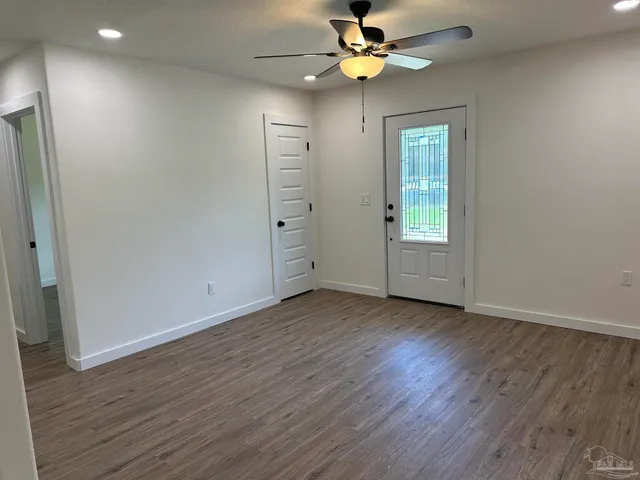 an empty room with wooden floor fan and windows