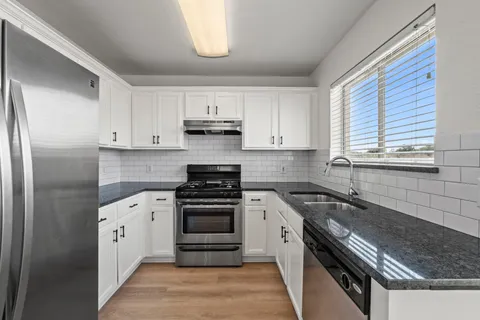 a kitchen with granite countertop a sink and a white wooden cabinets