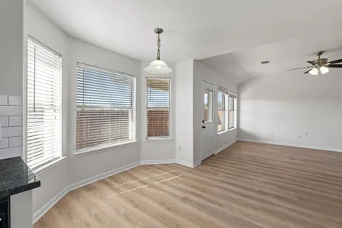 an empty room with wooden floor fan and windows