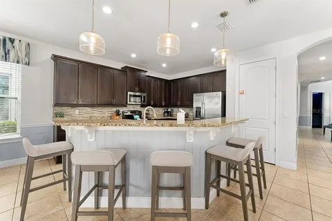 a kitchen with kitchen island granite countertop a dining table chairs refrigerator and microwave