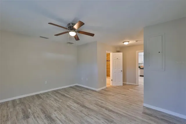 an empty room with wooden floor ceiling fan and windows