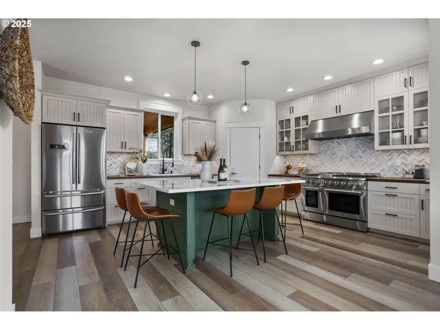 a kitchen with stainless steel appliances kitchen island granite countertop a stove a sink a refrigerator and a dining table with wooden floor