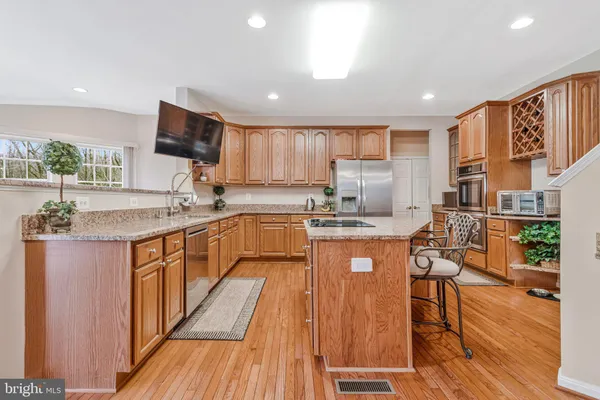 a kitchen with stainless steel appliances granite countertop wooden cabinets a sink dishwasher a stove and a refrigerator with wooden floor