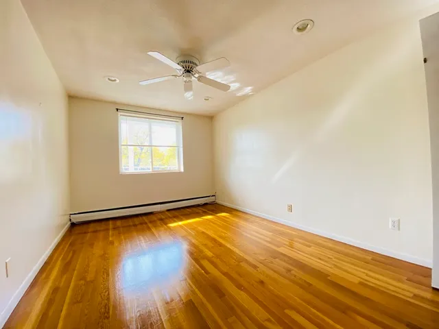 an empty room with wooden floor fan and windows