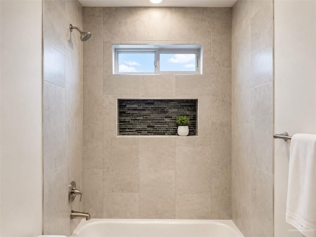 707 Palmer Road, Unit 3 Mission, TX 78573 - Photo 8 of 8 Bathtub shower combination featuring large format light-toned tile, a horizontal window, and a recessed niche with dark mosaic tile