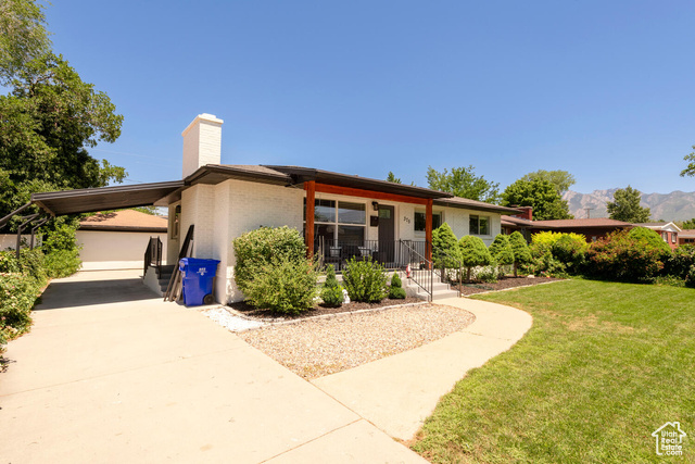 View of front of house with a front yard, a chimney, an attached carport, brick siding, and covered porch