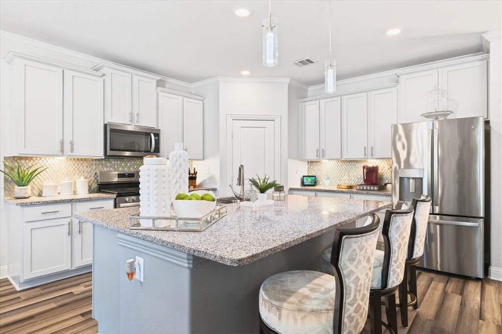 2816 Permian Road Aubrey, TX 76227 - Photo 11 of 36 Kitchen featuring stainless steel appliances, light stone counters, an island with sink, a breakfast bar, and crown molding