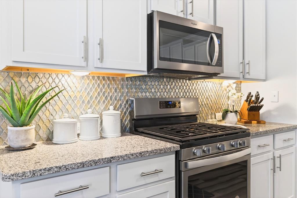 2816 Permian Road Aubrey, TX 76227 - Photo 12 of 36 Kitchen with stainless steel appliances, light stone counters, backsplash, and white cabinetry