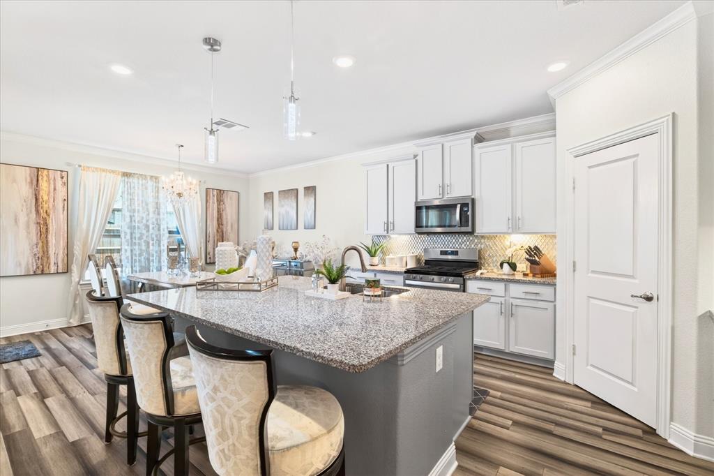 2816 Permian Road Aubrey, TX 76227 - Photo 3 of 36 Kitchen featuring stainless steel appliances, a breakfast bar area, an island with sink, light stone countertops, and dark wood-type flooring