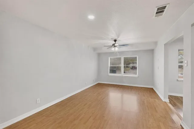 an empty room with wooden floor chandelier fan and windows