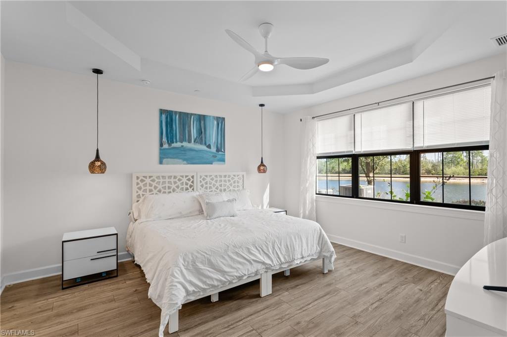9637 Montelanico Loop, Unit 104 Naples, FL 34119 - Photo 10 of 45 Bedroom featuring a raised ceiling, light wood-style flooring, ceiling fan, and a water view
