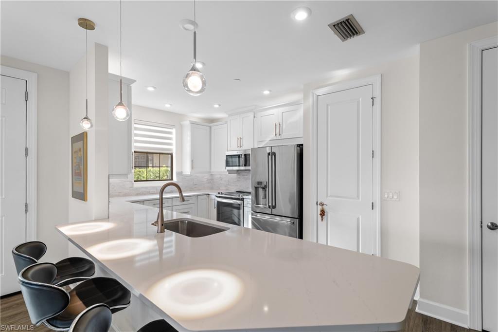 9637 Montelanico Loop, Unit 104 Naples, FL 34119 - Photo 6 of 45 Kitchen with decorative light fixtures, stainless steel appliances, a peninsula, white cabinets, and a breakfast bar area
