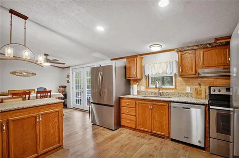 a kitchen with stainless steel appliances granite countertop a refrigerator a sink dishwasher a stove and white cabinets with wooden floor