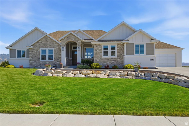 21 Pier Place Tooele, UT 84074 - Photo 1 of 112 Single-story residence featuring a stone and siding exterior with gabled rooflines, an arched entryway, an attached two-car garage, and a manicured front lawn with a natural rock retaining wall
