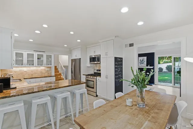 a kitchen with stainless steel appliances kitchen island granite countertop a refrigerator a stove a microwave oven with white cabinets and wooden floor