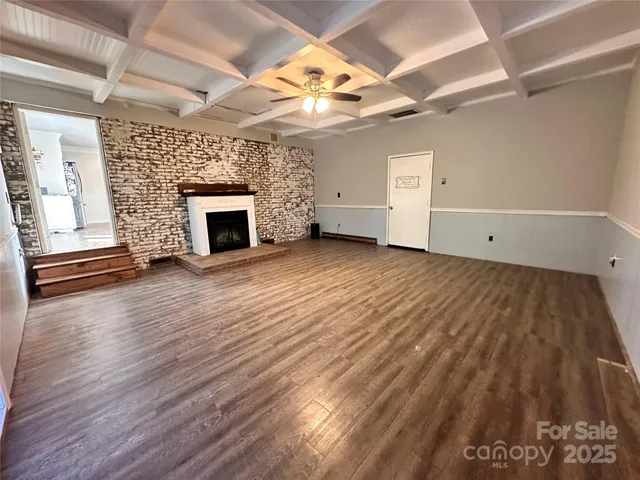 an empty room with wooden floor fireplace and windows