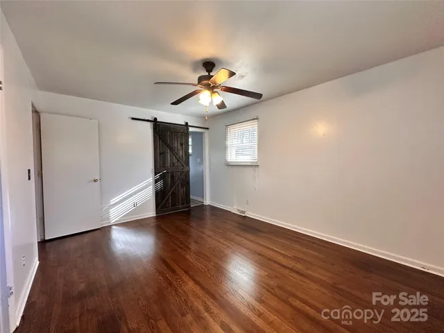 a view of an empty room with wooden floor and a ceiling fan