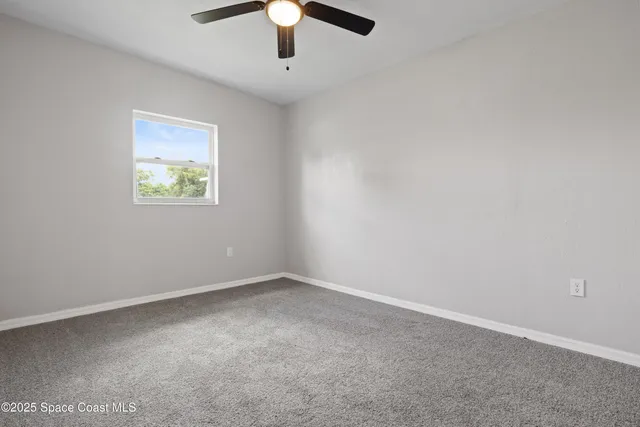 an empty room with a chandelier fan and windows