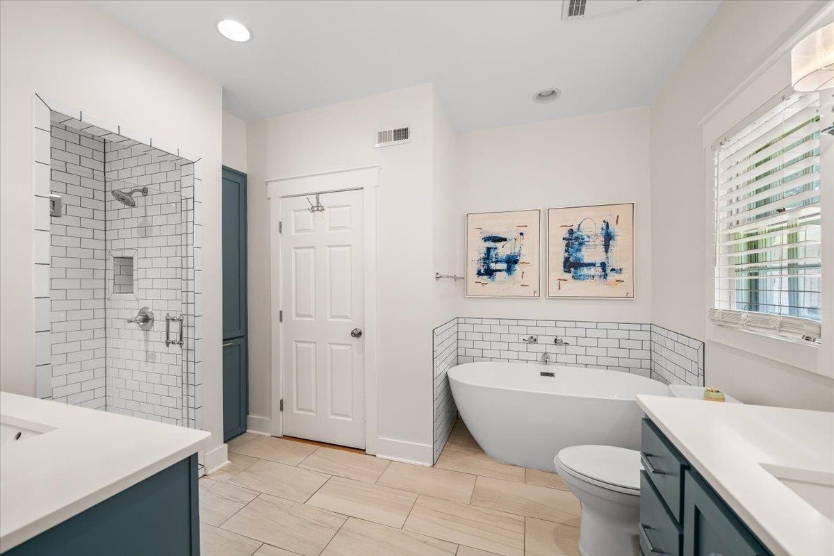 1273 Brookfield Road Memphis, TN 38119 - Photo 23 of 40 Stunning updated primary bathroom featuring a freestanding soaking tub, a frameless glass shower with subway tile surround, dual vanity sinks with white countertops, and light-toned tile flooring