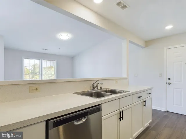 a utility room with stainless steel appliances a sink dishwasher and white cabinets with wooden floor