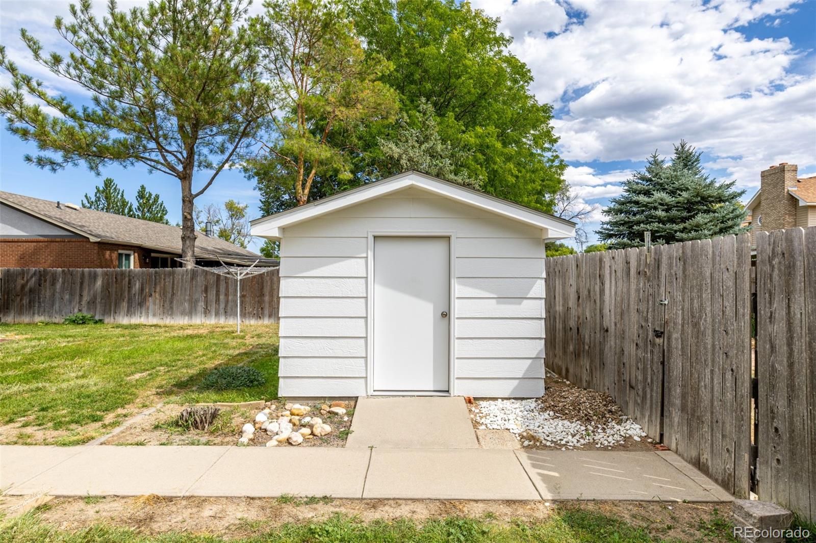 909 Fairhurst Street Sterling, CO 80751 - Photo 43 of 50 a white house with a small yard and large trees with wooden fence