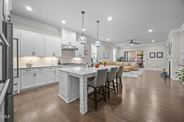 a kitchen with stainless steel appliances kitchen island granite countertop a stove a sink a refrigerator and white cabinets with wooden floor