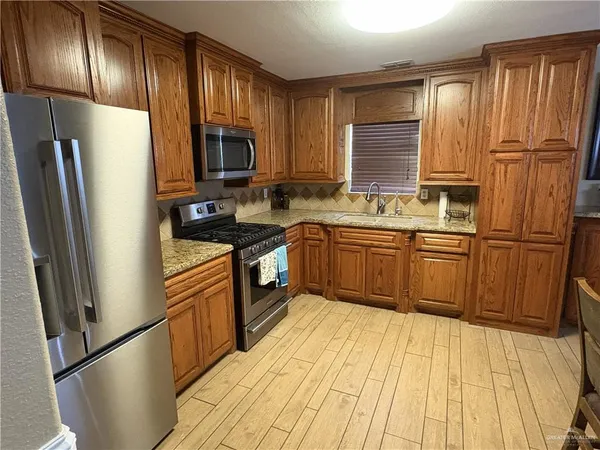 a kitchen with stainless steel appliances granite countertop a refrigerator a sink dishwasher a stove with wooden cabinets and floor