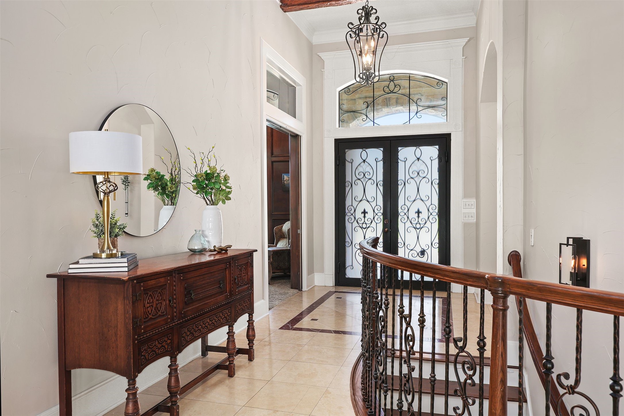 10896 Decatur Street Willis, TX 77318 - Photo 12 of 50 This elegant entryway welcomes you with a wrought iron double door featuring decorative glass, a stylish chandelier, and a beautifully crafted wooden console with a mirror, all set against neutral tones and complemented by a curved staircase with an ornate railing.