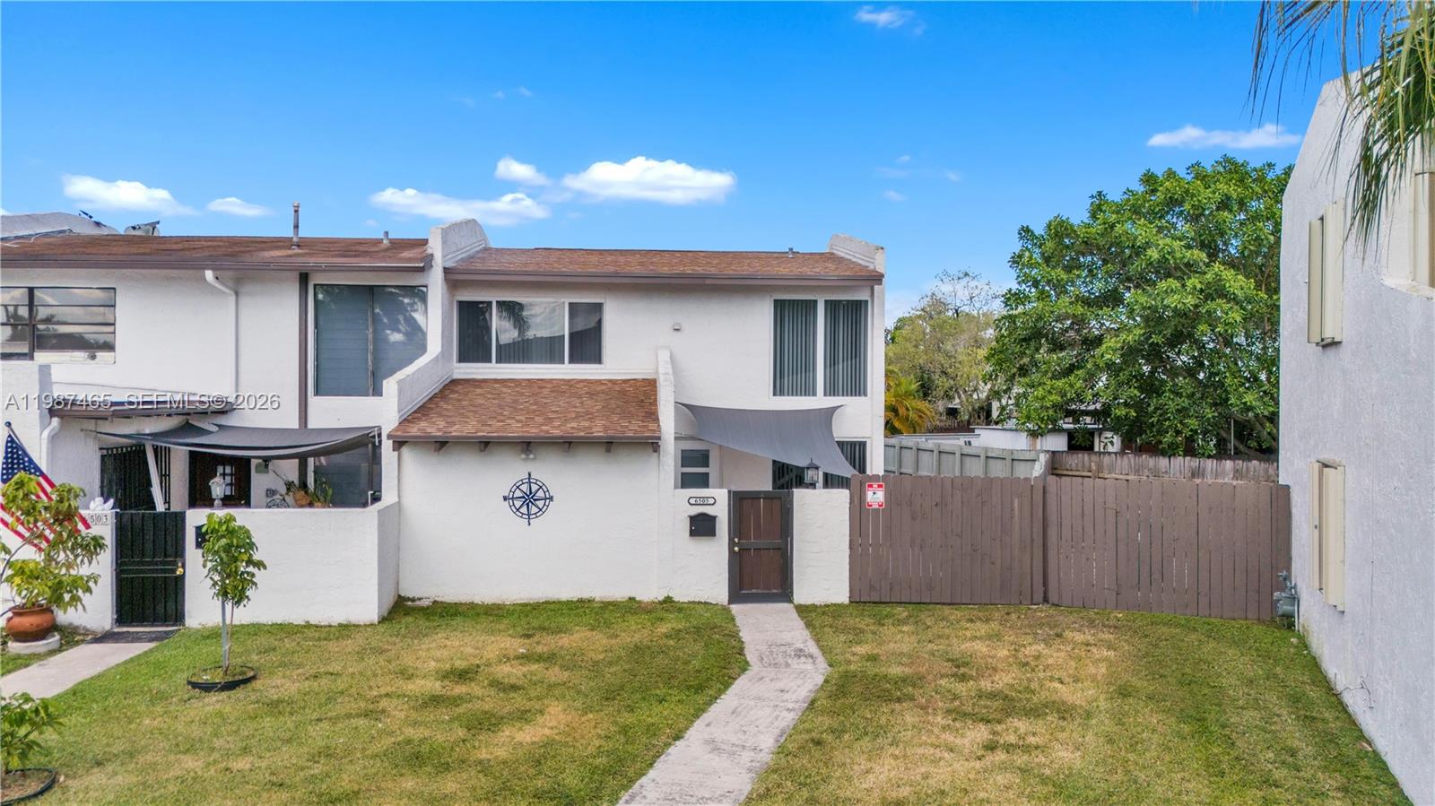 a view of a white house next to a yard with plants and trees