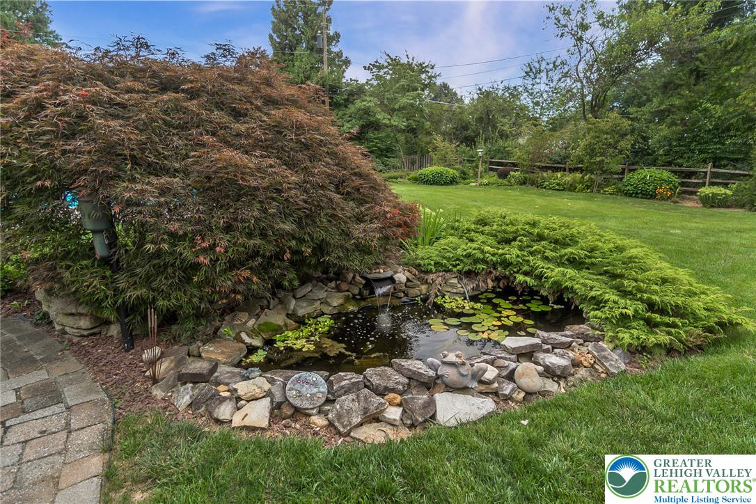 525 Wedgewood Road Bethlehem, PA 18017 - Photo 54 of 61 A tranquil garden oasis features a rock-lined pond with a gentle waterfall, nestled amidst lush landscaping and a well-maintained lawn.