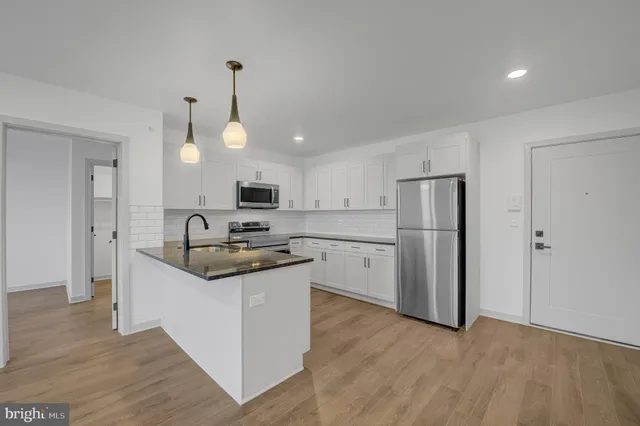 a kitchen with stainless steel appliances granite countertop a sink a stove a refrigerator and island with wooden floor