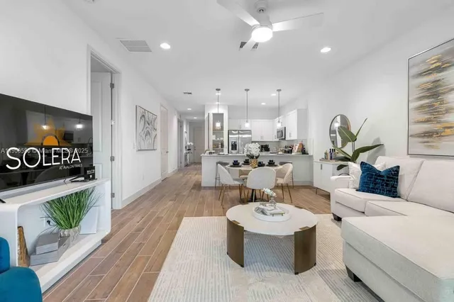 a open dining room with kitchen island stainless steel appliances granite countertop a sink a stove a refrigerator and a dining table with wooden floor