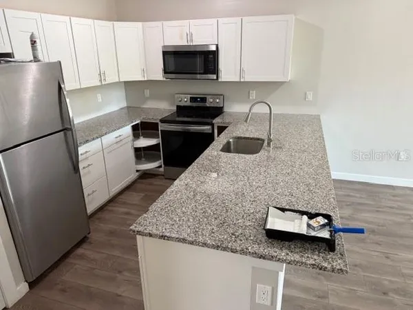 a kitchen with granite countertop a refrigerator a stove a sink and white cabinets