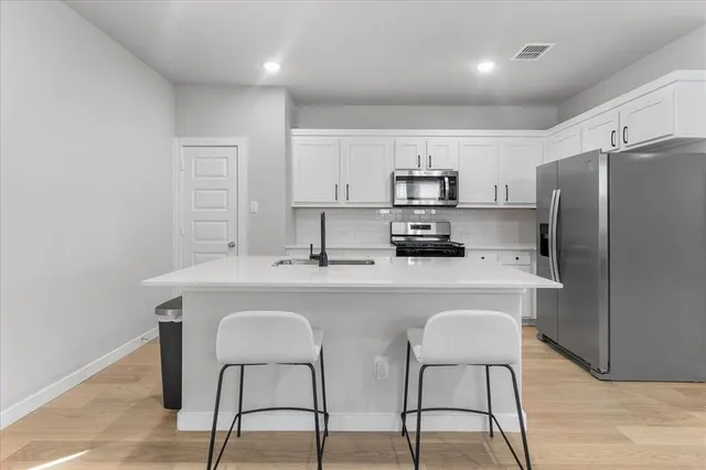 a kitchen with stainless steel appliances a dining table chairs refrigerator and sink