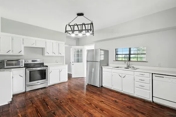 a kitchen with stainless steel appliances a stove a sink dishwasher a refrigerator and white cabinets with wooden floor