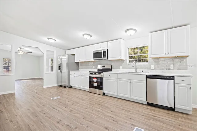 a kitchen with stainless steel appliances granite countertop a stove top oven a sink a refrigerator white cabinets and wooden floor