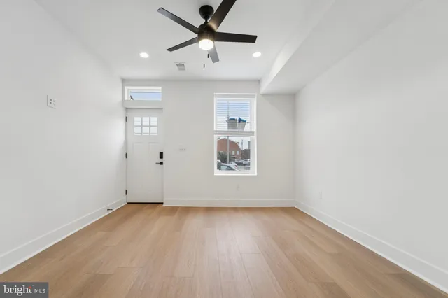 an empty room with wooden floor ceiling fan and windows