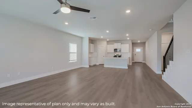 a view of an empty room with wooden floor kitchen view and a window