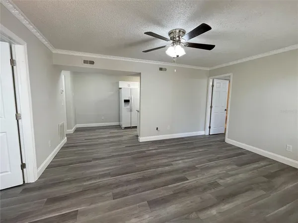 a view of an empty room with wooden floor and a ceiling fan