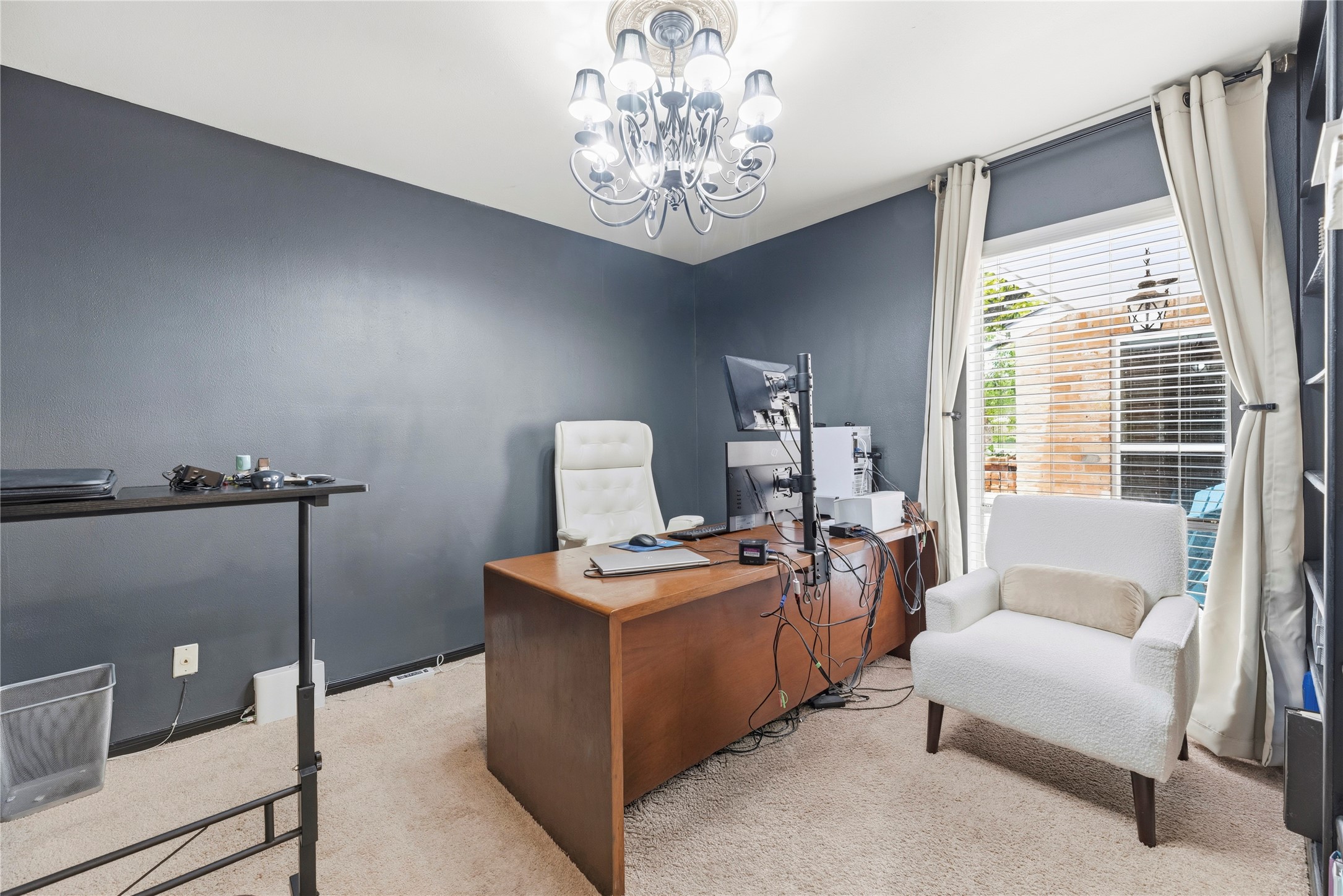 14203 Wickersham Lane Houston, TX 77077 - Photo 18 of 25 Versatile home office or bedroom space highlighted by a deep charcoal accent wall, plush carpeting, a multi-light chandelier fixture, and a large window providing views of the patio.