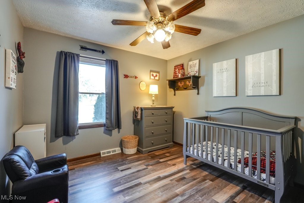 1157 Bass Circle Northwest Canton, OH 44708 - Photo 17 of 31 Bedroom featuring wood finished floors, baseboards, visible vents, a nursery area, and a textured ceiling