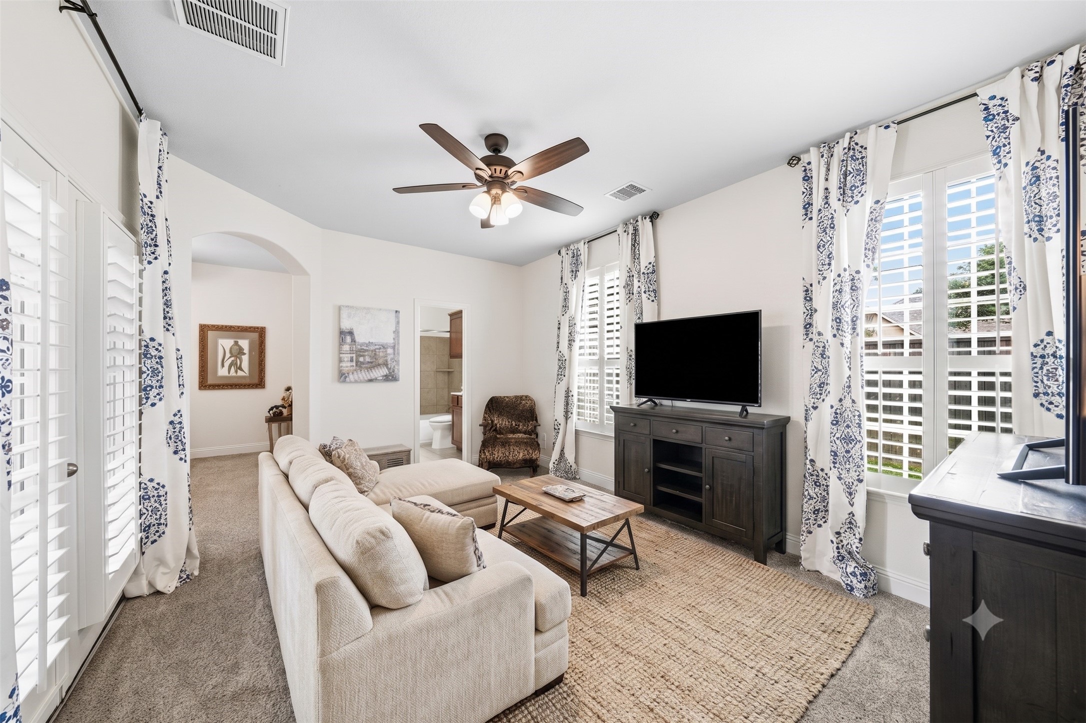 17610 Strackfield Lane Tomball, TX 77377 - Photo 28 of 50 Perfect for guests or multigenerational living, the private secondary suite begins with a charming sitting room filled with natural light, plantation shutters, elegant drapes, and direct access to the front porch through a 6-foot patio door. This photo has been virtually staged.