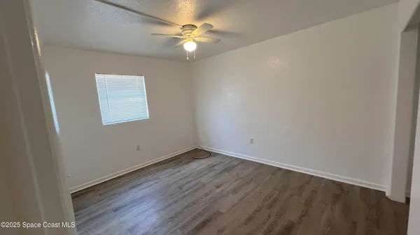 an empty room with wooden floor and fan